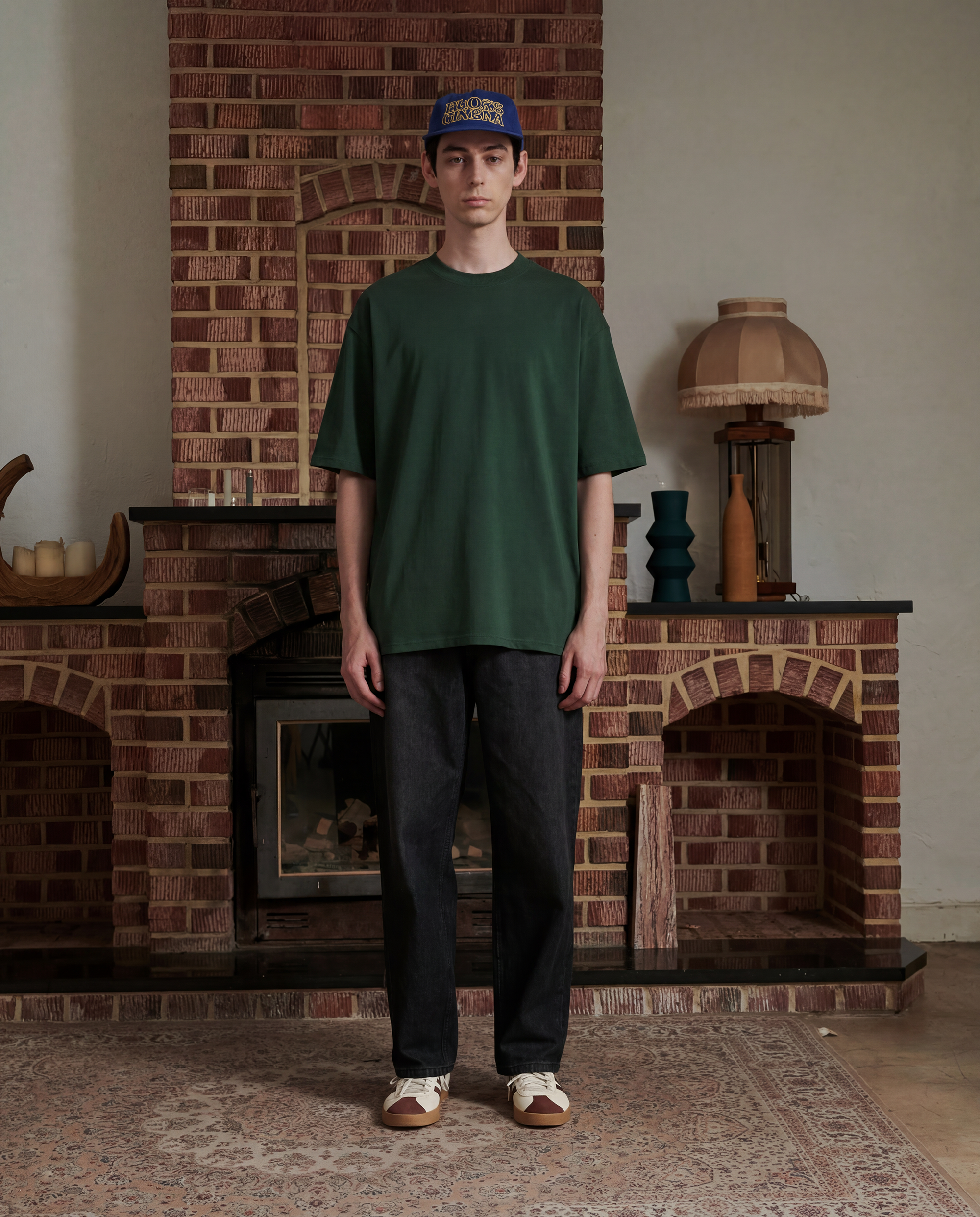 Person wearing a forest green shirt and dark pants standing in front of a brick fireplace.